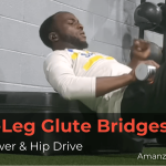 Soccer player performing single-leg glute bridge on a gym box with a dumbbell for hip strength and stability
