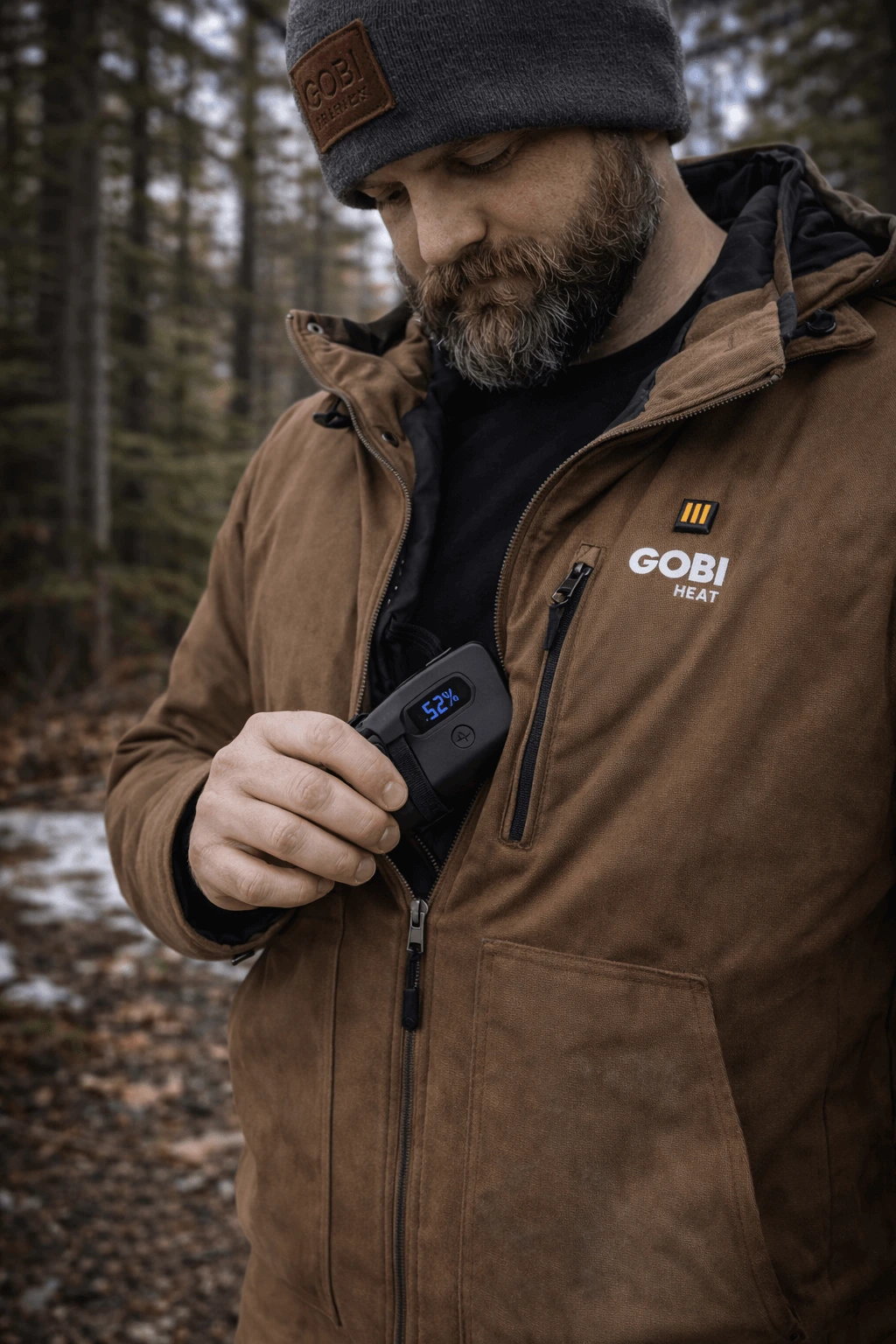 Worker checking Grit heated jacket battery inside chest pocket while wearing jacket outdoors in cold forest conditions