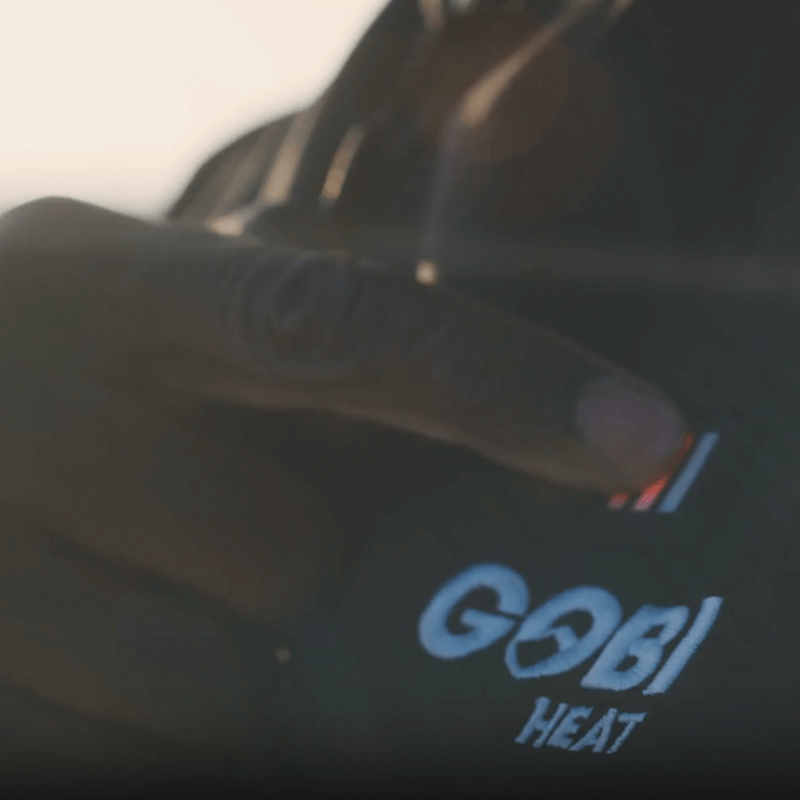 Person pressing three-bar power button on Gobi Heat Grit Heated Jacket to adjust heat levels