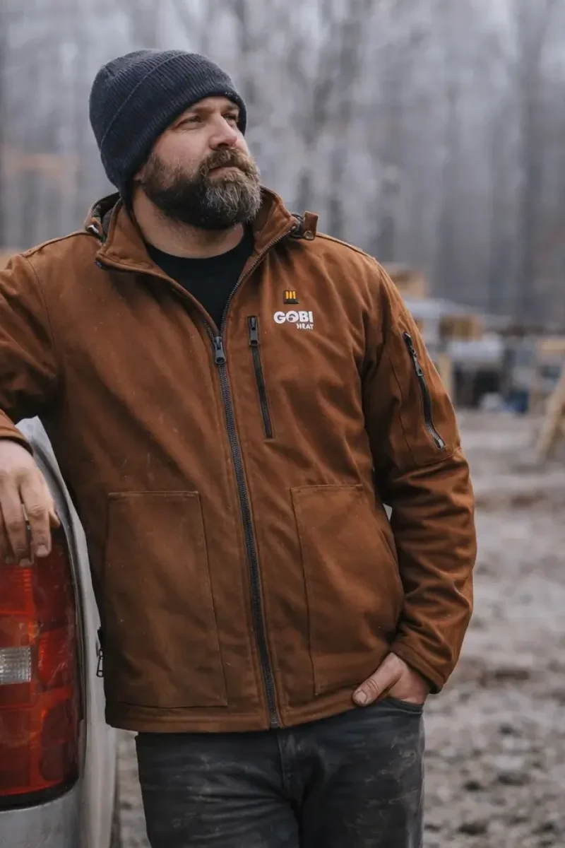 Tradesperson wearing the Grit heated jacket in grizzly color standing comfortably on a cold job site after a long work shift